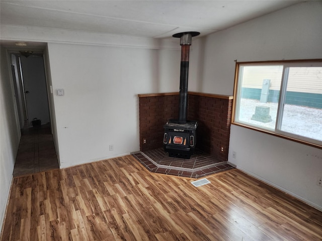 unfurnished living room featuring a wood stove, visible vents, and wood finished floors