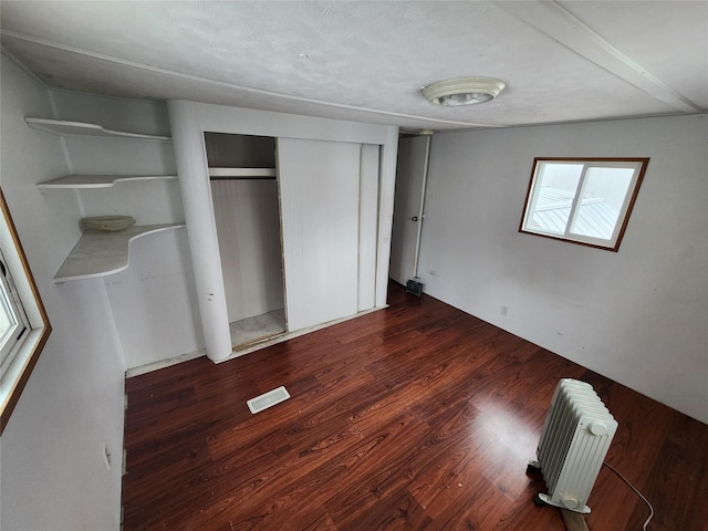 unfurnished bedroom featuring dark wood-style floors, radiator heating unit, visible vents, and a closet