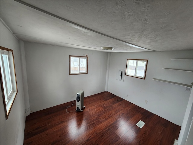 unfurnished room featuring a textured ceiling, dark wood-style flooring, visible vents, and a healthy amount of sunlight