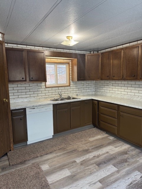 kitchen with dishwasher, sink, decorative backsplash, dark brown cabinets, and light wood-type flooring