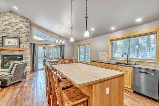 kitchen featuring dishwasher, sink, a kitchen breakfast bar, vaulted ceiling, and light brown cabinetry