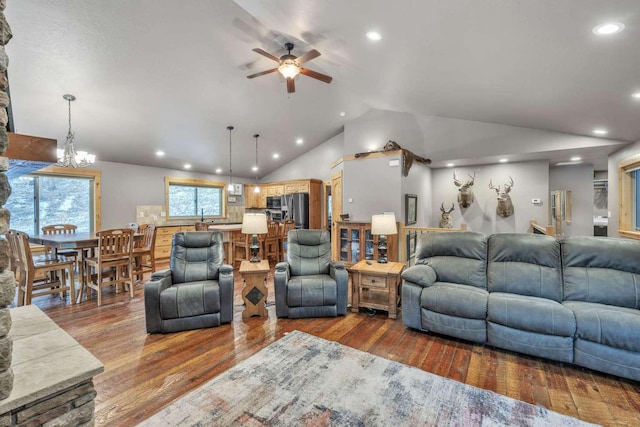 living room with ceiling fan with notable chandelier, hardwood / wood-style flooring, and vaulted ceiling