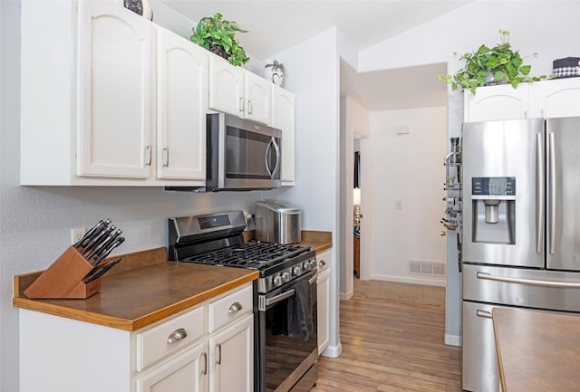 kitchen with stainless steel appliances, white cabinetry, and light hardwood / wood-style floors