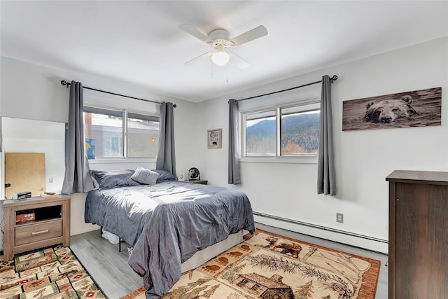 bedroom with light wood-type flooring, multiple windows, a baseboard heating unit, and ceiling fan