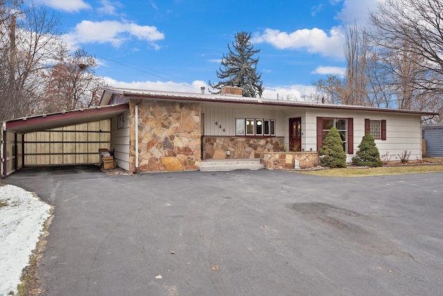 view of front of home with aphalt driveway, a chimney, stone siding, and a carport