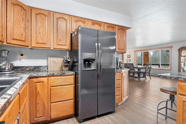 421 Tie Chute Ln, Florence, MT 59833 - kitchen with stainless steel fridge with ice dispenser, light wood-style floors, brown cabinetry, and dark countertops