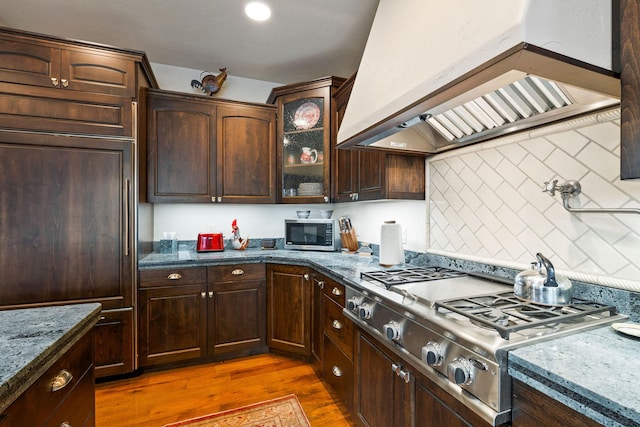 kitchen with decorative backsplash, dark stone counters, custom range hood, stainless steel appliances, and dark hardwood / wood-style floors