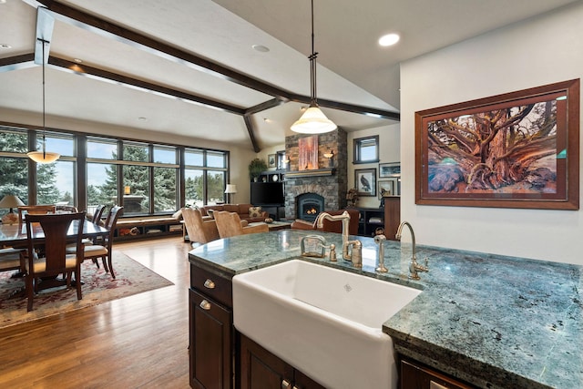 kitchen with pendant lighting, a stone fireplace, sink, vaulted ceiling with beams, and light wood-type flooring