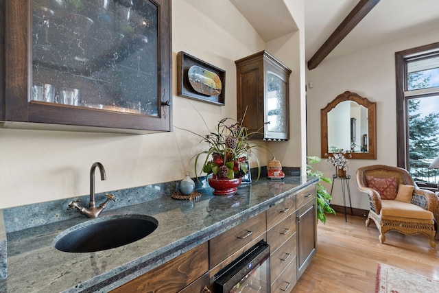 interior space featuring sink, dark stone countertops, light hardwood / wood-style floors, beam ceiling, and dark brown cabinetry