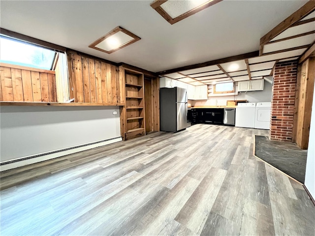 unfurnished living room with washing machine and clothes dryer, a baseboard heating unit, and light wood-type flooring