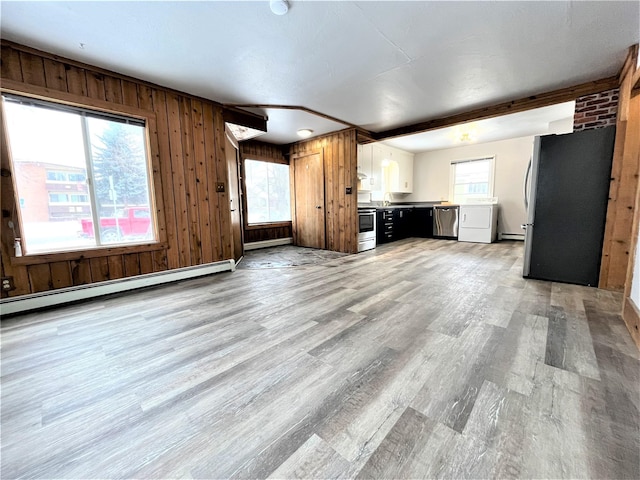 unfurnished living room featuring a baseboard radiator, plenty of natural light, and wood walls