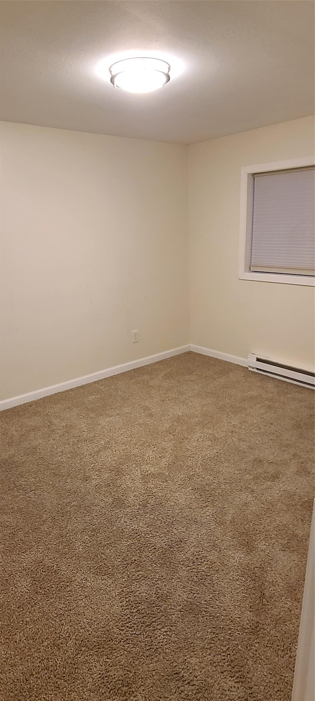 carpeted spare room with a baseboard heating unit