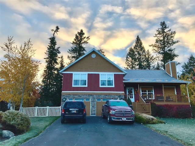 view of front of house with fence, driveway, a porch, an attached garage, and stone siding