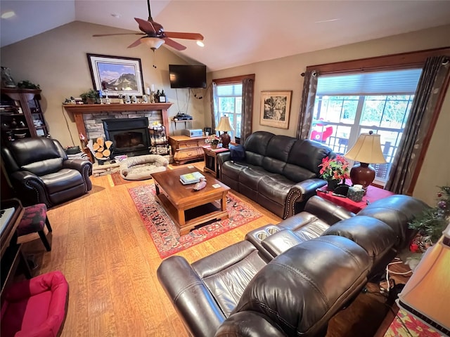 living room with hardwood / wood-style flooring, ceiling fan, a stone fireplace, and vaulted ceiling