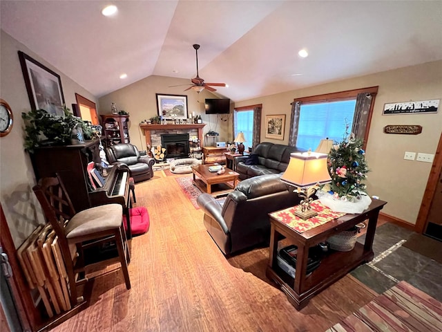 living room with a stone fireplace, ceiling fan, vaulted ceiling, and hardwood / wood-style flooring