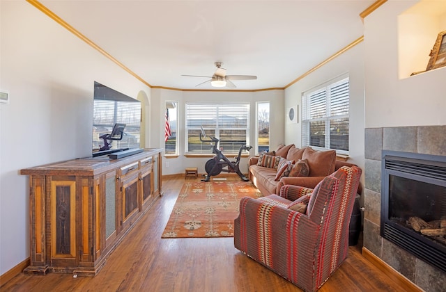 living room featuring ceiling fan, dark hardwood / wood-style flooring, ornamental molding, and a tiled fireplace