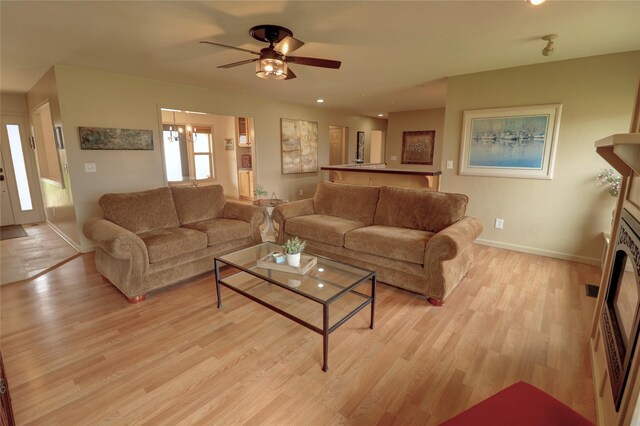 living room featuring ceiling fan with notable chandelier and light hardwood / wood-style floors