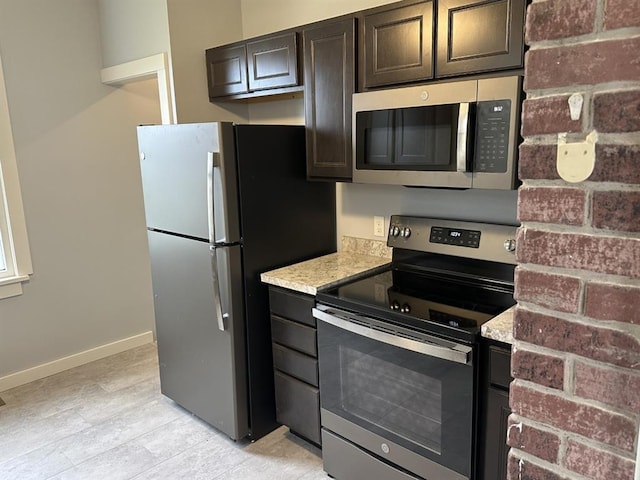 kitchen with dark brown cabinetry, light stone countertops, and stainless steel appliances