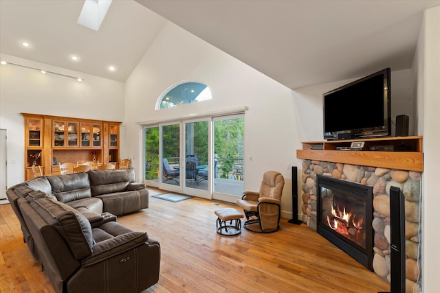 living room with a fireplace, light hardwood / wood-style floors, high vaulted ceiling, and a skylight