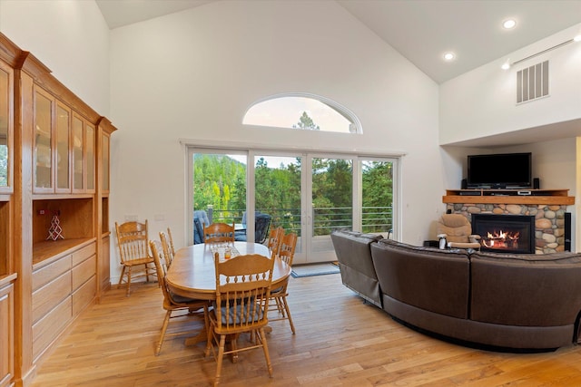 dining room with a stone fireplace, high vaulted ceiling, and light hardwood / wood-style flooring