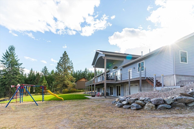 back of property featuring a deck, a patio area, a playground, a garage, and a lawn