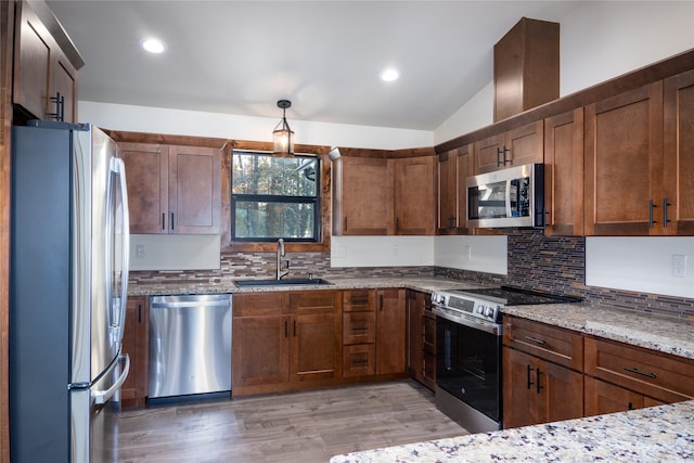 kitchen with lofted ceiling, sink, light stone countertops, light wood-type flooring, and stainless steel appliances