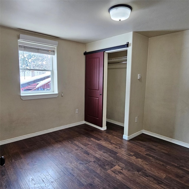 unfurnished bedroom featuring a closet, a barn door, and dark hardwood / wood-style flooring