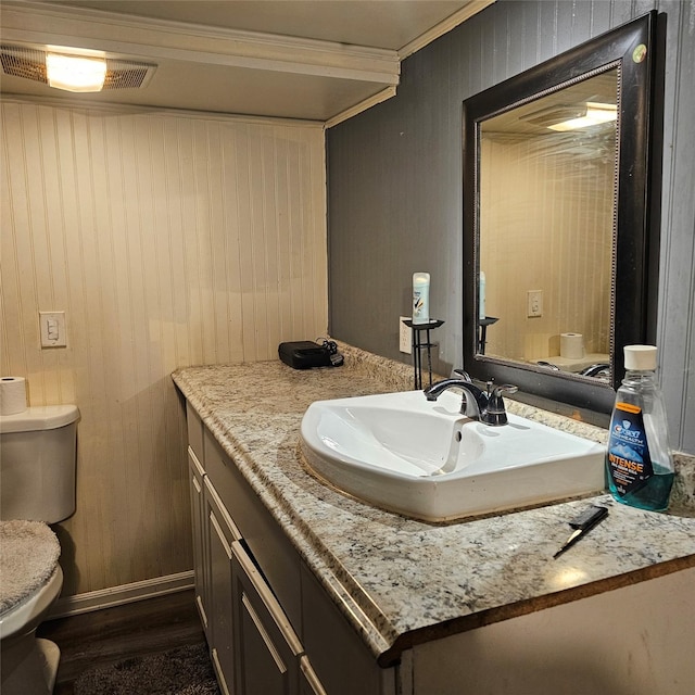 bathroom with wood walls, toilet, vanity, ornamental molding, and hardwood / wood-style flooring