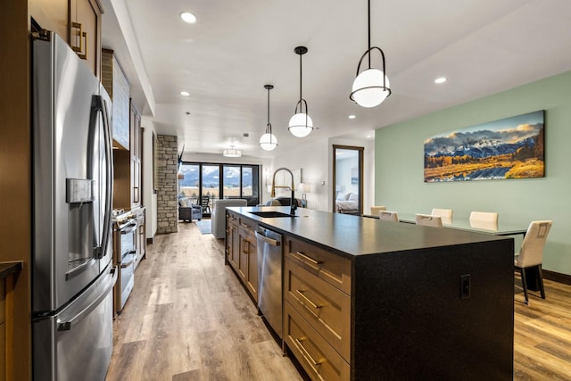 kitchen with sink, an island with sink, decorative light fixtures, light hardwood / wood-style floors, and stainless steel appliances