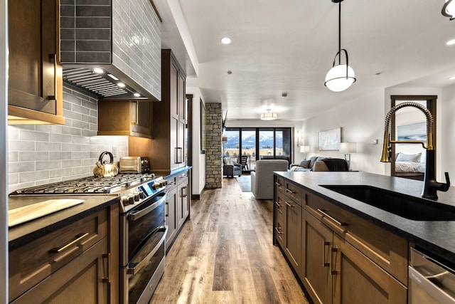 kitchen featuring appliances with stainless steel finishes, a sink, wall chimney range hood, dark countertops, and decorative backsplash