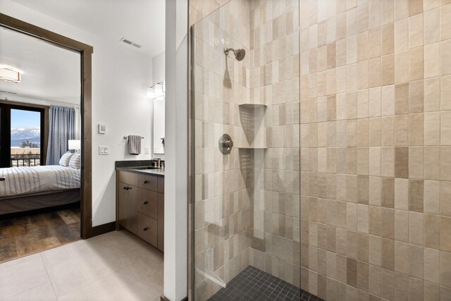 ensuite bathroom featuring tiled shower, vanity, and tile patterned floors