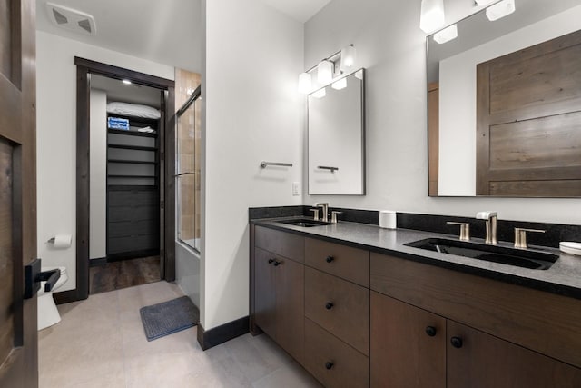 bathroom featuring baseboards, double vanity, and bath / shower combo with glass door