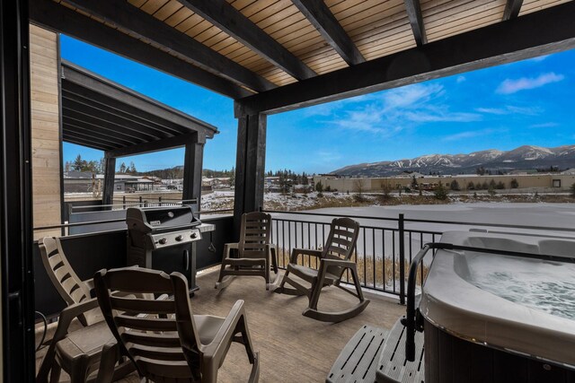 snow covered patio featuring a mountain view, a hot tub, area for grilling, and a balcony