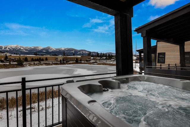 snow covered patio with a mountain view, a balcony, and a hot tub