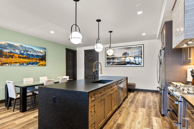 kitchen featuring a center island with sink, sink, hanging light fixtures, light wood-type flooring, and stainless steel appliances