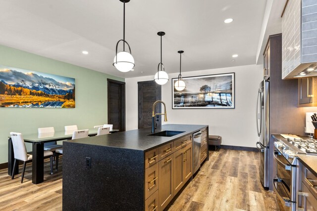 kitchen with stainless steel appliances, a sink, dark countertops, light wood-style floors, and recessed lighting