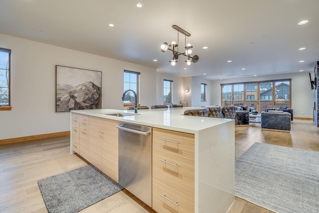 kitchen with light brown cabinets, a large island with sink, sink, light wood-type flooring, and a notable chandelier