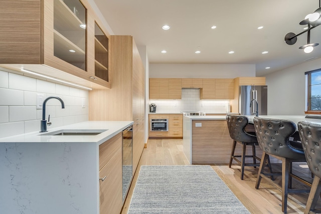 kitchen featuring decorative backsplash, a kitchen bar, light wood-type flooring, stainless steel fridge, and sink