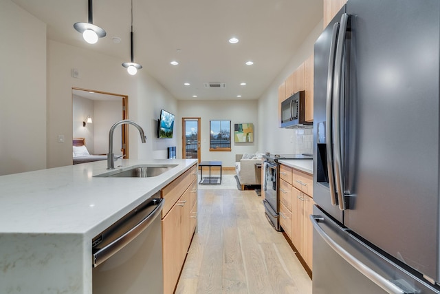 kitchen with pendant lighting, a kitchen island with sink, sink, light hardwood / wood-style flooring, and appliances with stainless steel finishes