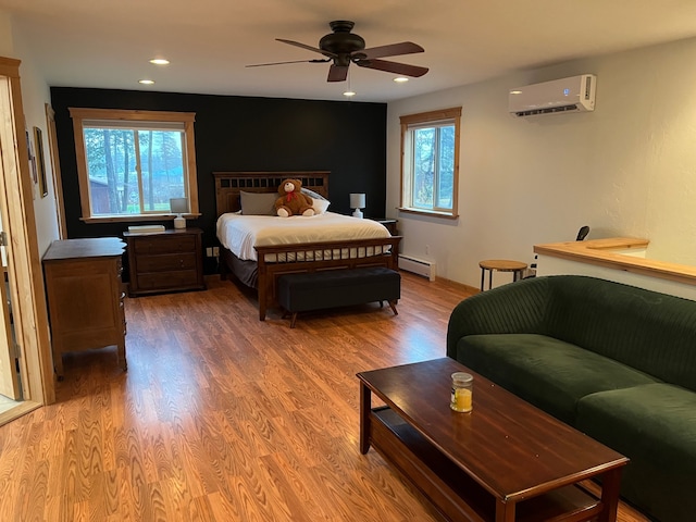 bedroom featuring hardwood / wood-style flooring, an AC wall unit, baseboard heating, and multiple windows