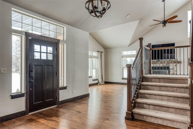 foyer featuring baseboards, stairway, wood finished floors, vaulted ceiling, and ceiling fan with notable chandelier