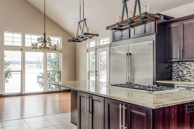 kitchen featuring stainless steel appliances, a kitchen island, decorative backsplash, light stone countertops, and decorative light fixtures