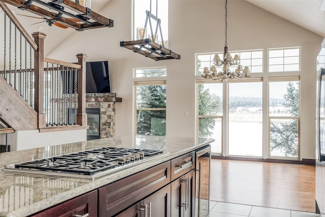 kitchen with a stone fireplace, wine cooler, light stone counters, stainless steel gas cooktop, and ceiling fan with notable chandelier