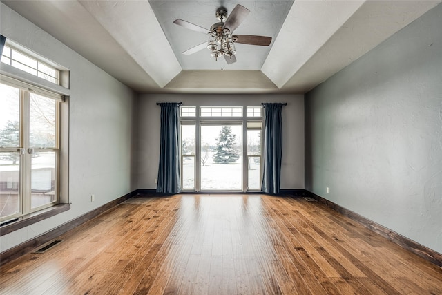 empty room with wood-type flooring, visible vents, plenty of natural light, and a raised ceiling