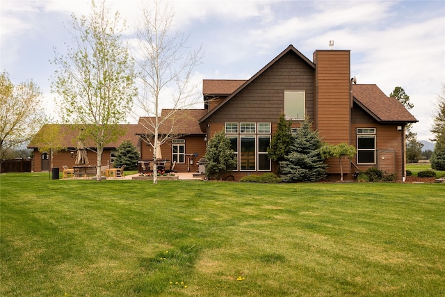 back of house with a shingled roof, a yard, a chimney, and a patio