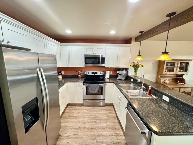 kitchen featuring appliances with stainless steel finishes, sink, light hardwood / wood-style floors, white cabinetry, and hanging light fixtures