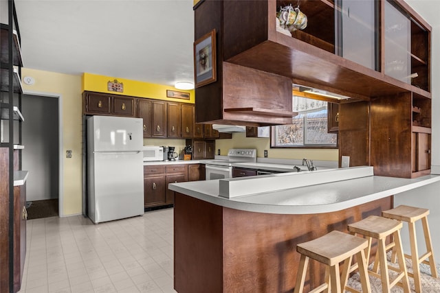 kitchen featuring a breakfast bar, dark brown cabinetry, white appliances, and kitchen peninsula