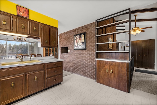 kitchen featuring brick wall, dark brown cabinets, ceiling fan with notable chandelier, sink, and vaulted ceiling with beams