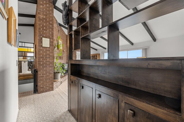 bar with dark brown cabinetry, light colored carpet, and vaulted ceiling with beams