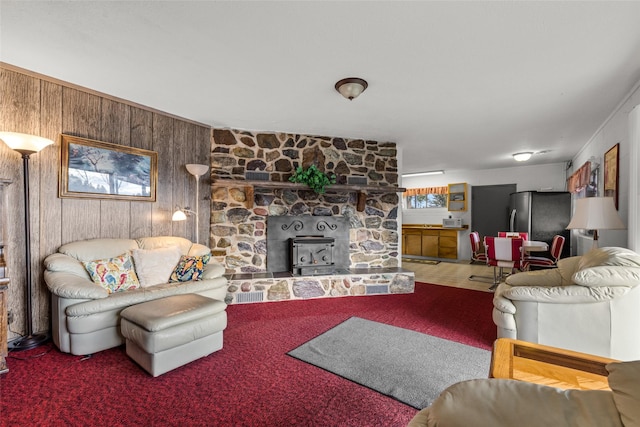 carpeted living room featuring wood walls and a wood stove